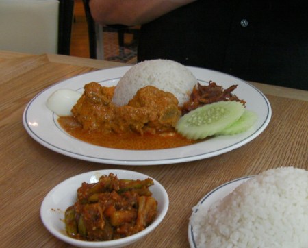 plate containing rice, curry chicken, spicy anchovies, cucumbers, a hard boiled egg and spicy pickles