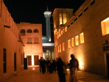 people walking through traditional Arab buildings toward a mosque