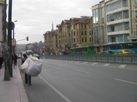 main street with tram line down the middle and a man carrying a large sack on his back