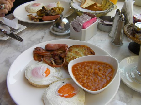 American breakfast plate of 2 eggs, bacon, potato cake and bowl of beans