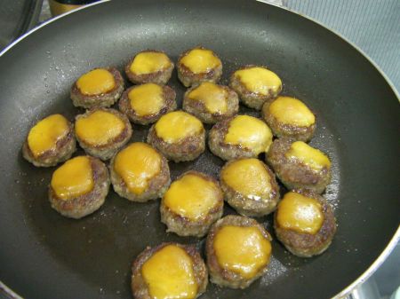 frying pan full of bite-sized burgers with a little square of cheese on top
