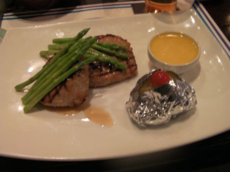 rectangular white plate with two pork cutlets, asparagus, baked potato, herb butter.