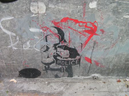 Street Art in Athens stencil of riot policeman pointing gun directly at the viewer
