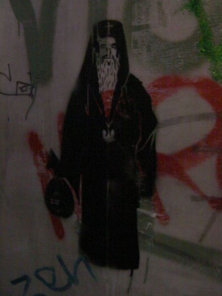 stenciled graffiti of a priest holding a bag of money and giving the finger