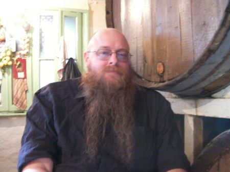 bearded man sitting next to a large wine barrel