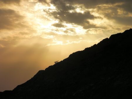 sun shining through clouds over a hill
