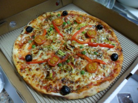 pizza topped with six olives, some tomatoes, green peas