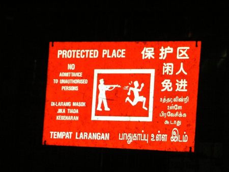 warning sign showing one figure aiming a gun at another figure running away