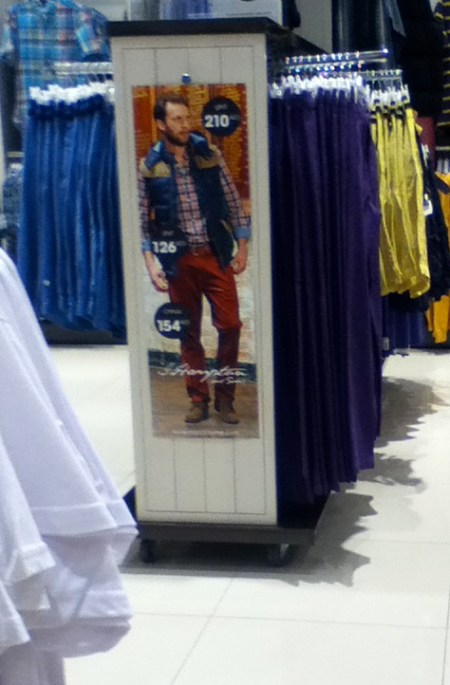 department store poster showing a male model wearing a plaid shirt and a sleeveless down vest