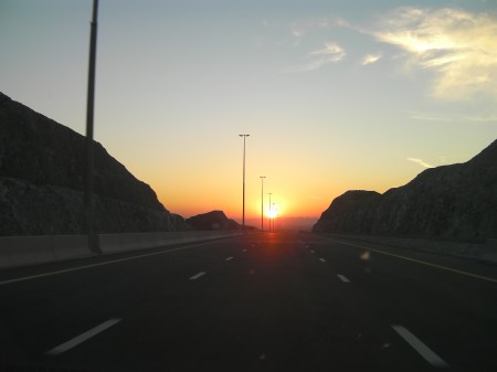 red sunset as viewed from a highway between rugged hills