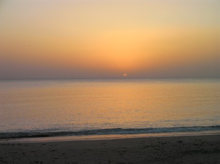 ocean, orange haze, small arc of the sun appearing