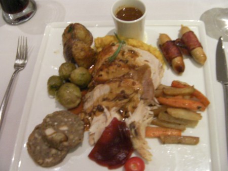 plate of turkey slices, brussel sprouts, carrots, sausages, potatoes, stuffing, cranberry sauce