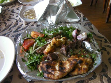plate wrapped in aluminum foil containing mixed grilled meats