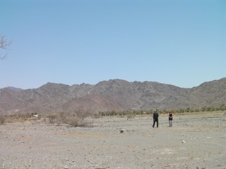 mountains in the distance, flat desert area in the foreground, two people walking