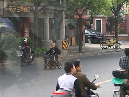 an elderly man in an electric wheelchair traveling down the street