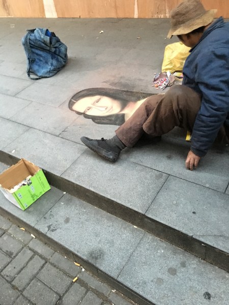 homeless man drawing the Mona Lisa in chalk on the sidewalk