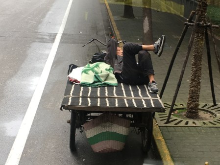 man relaxing on the bed of his three wheeled bicycle cart, looking at his smart phone
