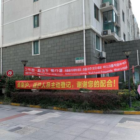 red banners at apartment entrance stating "reduce outdoor activities, wash hands frequently, wear a mask" in four languages