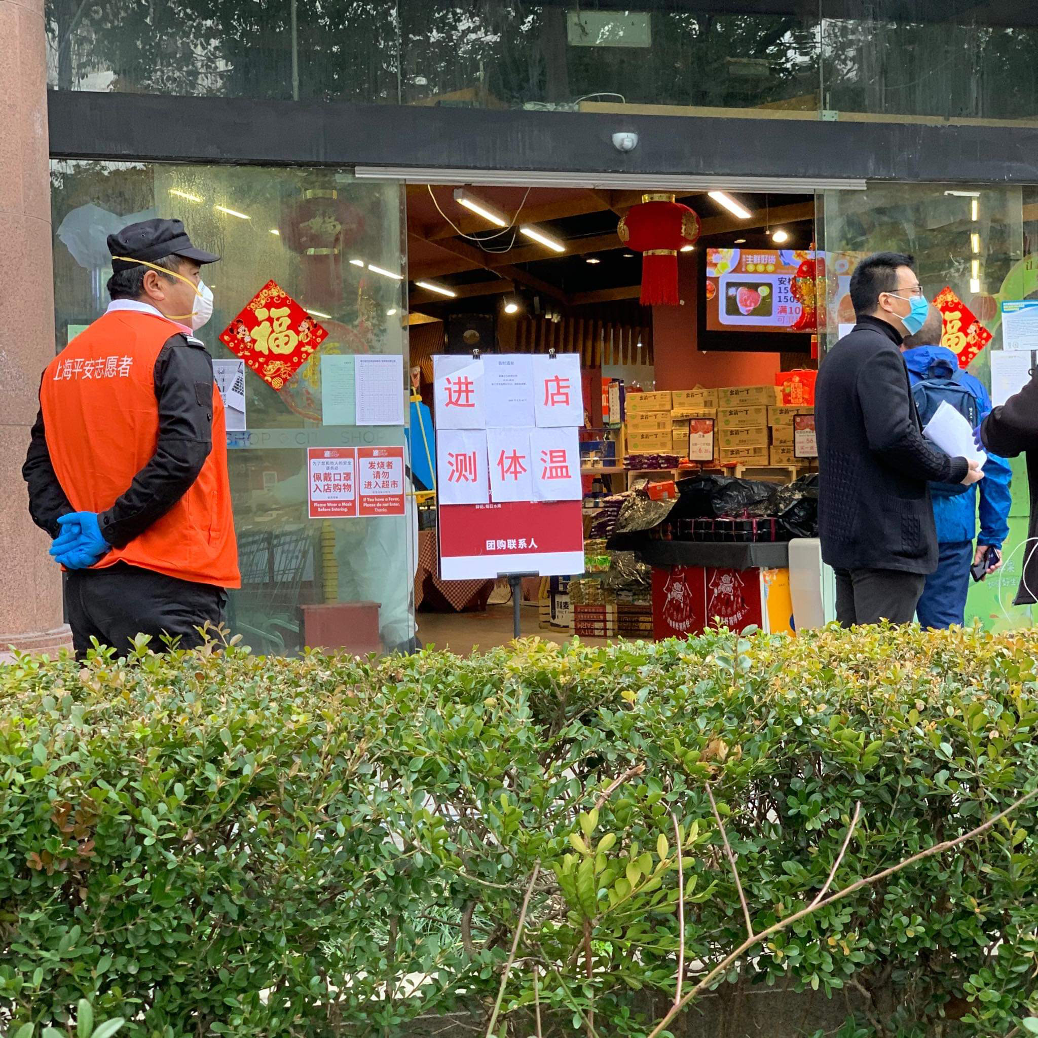 grocery store entrance with warning signs and people in medical masks and gloves.