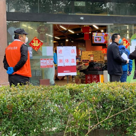 grocery store entrance with warning signs and people in medical masks and gloves.