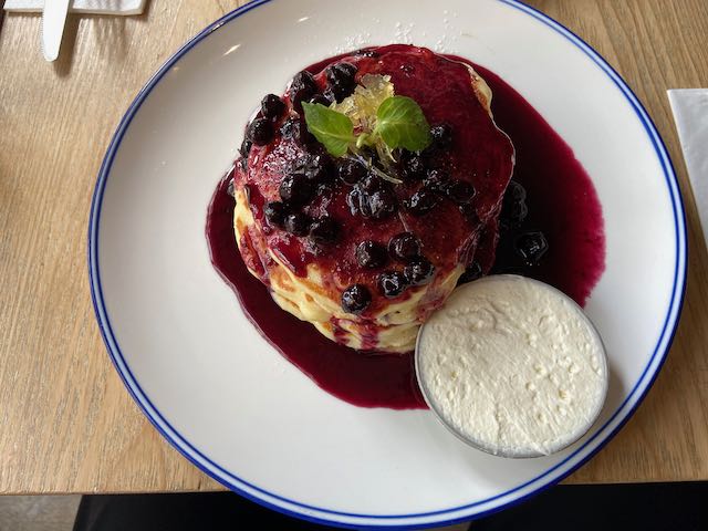 blue berry pancakes with blue berry syrup and whipped cream on the side