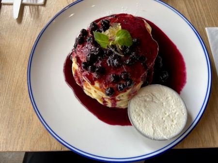 blue berry pancakes with blue berry syrup and whipped cream on the side