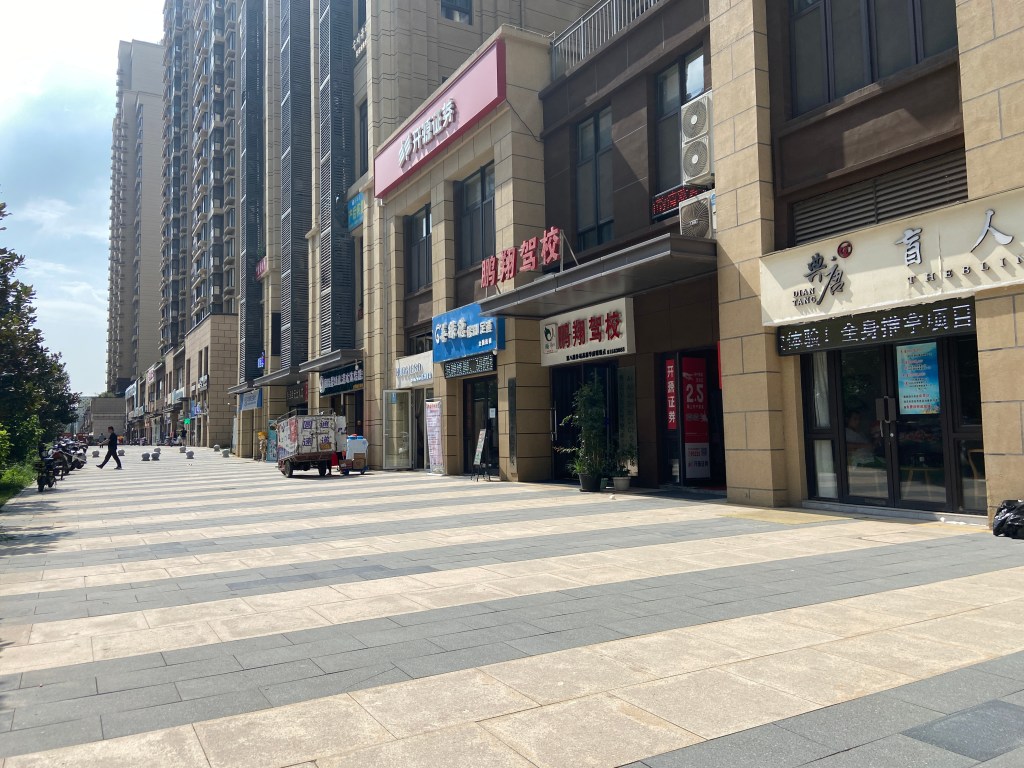 broad sidewalk lined with multiple small shops and tall apartment buildings