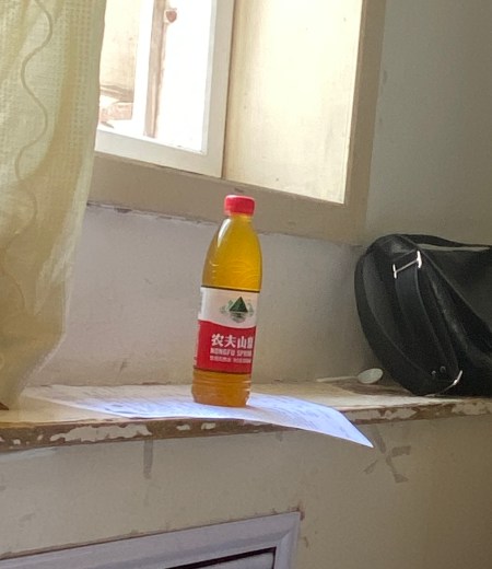 reused water bottle containing yellow fluid sample on a warn wooden shelf below a window